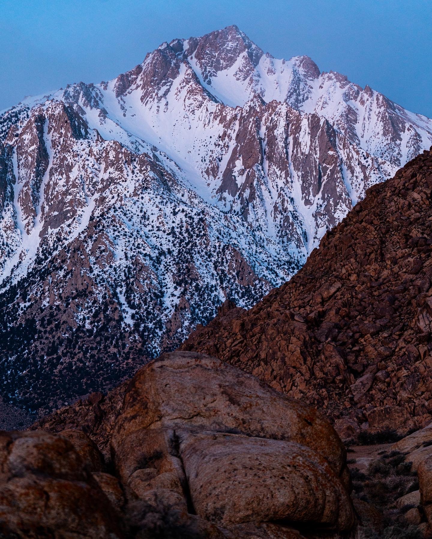 Snow-capped mountain peak at dusk with rocky foreground